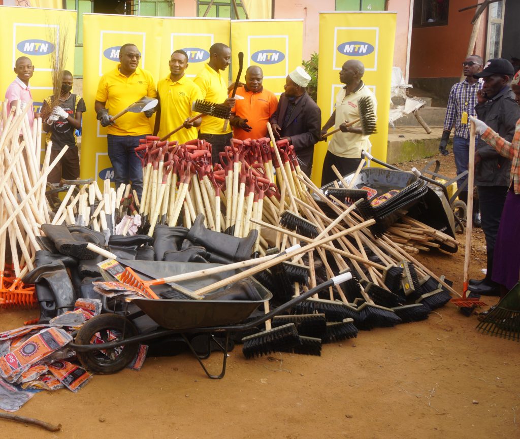 A team of MTN Staff and residents of Masaka City stand before the equipment donated to Masaka City to enable maintanance and hygiene of the area through the clean up exercise