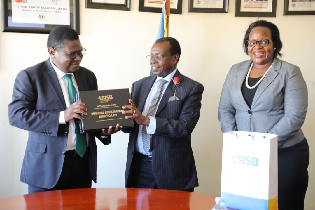 Hon.Norbert Mao Justice Constitutional Affairs Minister receives a compedium of laws from Amb.Francis Butagira URSB Board Chair. Looking on is Mercy K. Kainobwisho Registrar General.