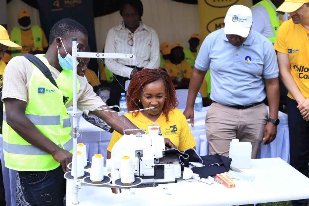 MTN Uganda CEO Sylvia Mulinge in yello T shirt tests sewing machines donated to the Disability Employment Link Project Uganda located in Bwaise Kampala as part of this years MTNS 21 Days of Yello Care